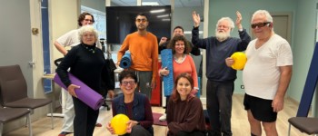 Huit personnes posent ensemble dans une salle de sport, certaines tenant des tapis de yoga ou des ballons. Elles sourient à la caméra, illustrant un atelier collectif de renforcement musculaire dans une atmosphère conviviale.