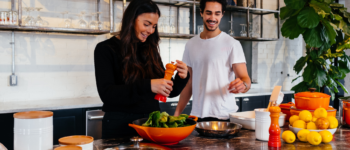 Photographie d’un atelier de cuisine : une femme sale une salade, un homme se tient à côté d’elle et s’apprête à lui passer le poivrier