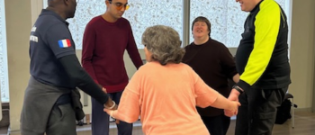 Un groupe de cinq membres se tient en cercle dans une salle, se tenant les mains et souriant pendant une activité collective.