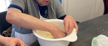 Un homme mélange une pâte dans un grand saladier blanc posé sur une table.