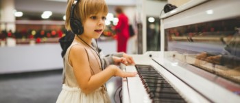 une enfant joue du piano avec un casque sur les oreilles, elle semble émerveillée