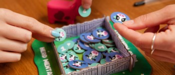 photo d'un plateau du jeu MEUH ! sous forme de pré à vache avec une vache rose et des pions avec des vaches dessinés dessus que des mains tiennent