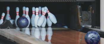 photo d'une balle de bowling arrivant sur des quilles qui commencent à tomber sur une piste de bowling