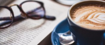 photo d'un café et d'un livre posés sur une table avec des lunettes posées sur le livre