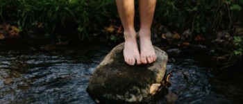 Une personne pieds nus se tient sur un rocher dans une rivière