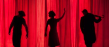 photo de silhouettes sur une scène derrière un rideau rouge dans un théâtre, deux dansent et une joue du violon